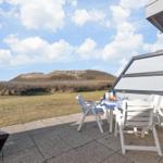Terrace with table and chairs, view of dunes and sky.