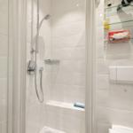 Shower with glass enclosure, showerhead, and shelf with tissue box and hair dryer.