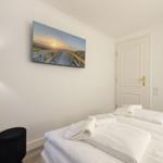 Bedroom with bed, towels, and wall art. Door and nightstand visible.