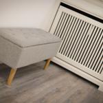 Gray ottoman with wooden legs next to heater