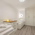 Room with two beds, wardrobe, and wooden floor.