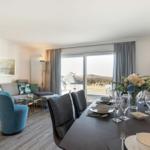 Dining area with table and chairs, living area with sofa and armchair, view of terrace and landscape.