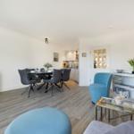 Living and dining area with dining table, blue chairs, and kitchen area.