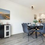 Dining area with table, chairs, and kitchen. Wall art shows beach.