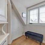 Ein Raum mit Dachschräge, Fenster mit Jalousien, blauer Sitzbank und weißer Einbauschränke.