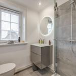 Badezimmer mit Dusche, Waschbecken und Toilette. Fenster mit Jalousie.