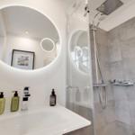 Badezimmer mit runden Spiegel, Dusche und Waschbecken mit Seifenflaschen.