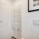 Helle Toilette mit Heizkörper, Spiegel und Bild an der Wand.