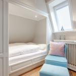 Ein Schlafzimmer mit Dachschrägen, weißem Bett und blauem Sessel.