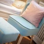 Ein hellblauer Sessel mit Kissen und Hocker neben dem Bett.
