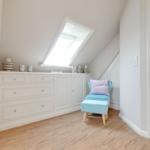 Schlafzimmer mit Dachschrägen, weißem Schrank und blauem Sessel.