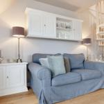 Ein Wohnzimmer mit blauem Sofa, weißen Schränken und einer weißen Wendeltreppe.