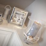 Auf einem Schrank stehen ein Bilderrahmen, eine Kerze und Meeresmuscheln.