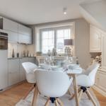 Küche mit Essbereich, weißer Tisch und Stühle, Fenster mit Jalousien und moderner Einbauküche.