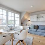 Essbereich mit Tisch und Stühlen, Wohnbereich mit Sofa und Schrank an der Wand.