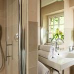 Badezimmer mit Dusche, Waschbecken und Fenster mit Blumen.