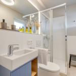 Badezimmer mit Dusche, Waschbecken und Toilette. Weiße Fliesen und moderne Einrichtung.