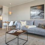 Wohnzimmer mit Sofa, Esstisch und Küchenbereich. Wandbild und Beleuchtung sichtbar.