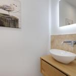 Waschbecken auf Holzschrank mit Spiegel und Wandbild.