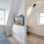 Schlafzimmer mit Dachschräge, Fenster und TV. Nebenraum mit Sessel und Fenster.