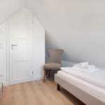 Zimmer mit Doppelbett, Stuhl und Tür unter Dachschräge.