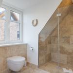 Badezimmer mit Dusche, Toilette und Fenster mit Blick auf Hauswand.