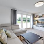Wohnzimmer mit Sofa, Fernseher und großen Fenstern.