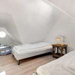 Zimmer mit zwei Betten, Holzboden und runder Fensteröffnung unter Dachschrägen.
