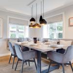 Dining room with wooden table, gray chairs, and windows with view of green.