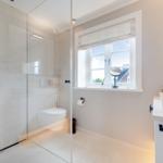 Bathroom with shower, toilet, and sink. Window with roller blind.