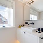 Bathroom with sink, mirror, and window overlooking a house.