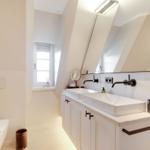 Bathroom with two sinks, mirror, and shower under sloped ceiling.