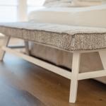 A white bench with patterned upholstery is placed at the foot of a bed.
