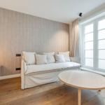 A room with sofa, round table, and large window. Patterned wall, wooden floor, and pendant lamp.