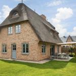 House with thatched roof and garden with table and umbrella.