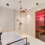 Shower with rain shower and bathtub, next to sauna with wooden bench.