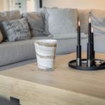 Wooden table with cup and lit candles in front of a sofa.