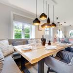 Dining area with wooden table, bench, and pendant lights. Kitchen in background.