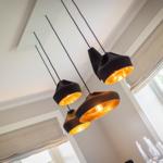 Suspended lamp with four black-golden shades over a dining area with window.
