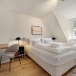 Schlafzimmer mit Doppelbett, Schreibtisch und Fenster mit Blick auf Grün.