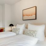 Schlafzimmer mit Bett, Kissen, Wandbild und runder Spiegel an der Wand.