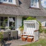 Haus mit Strohdach, Terrasse mit Esstisch, Strandkörben und Garten.