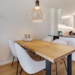 Essbereich mit Holztisch, Stühlen und Deckenleuchte. Küche mit Arbeitsplatte und Fenster.