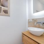Waschbecken auf Holzunterschrank mit Spiegelschrank und Wandbild mit Muscheln.
