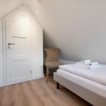 Schlafzimmer mit Dachschrägen, Bett, Stuhl und Tür.