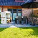 Terrasse mit Sitzgruppe, Sonnenschutz und Strandkorb vor Haus mit Backsteinmauer.