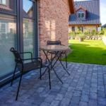 Terrasse mit Tisch und Stühlen neben Backsteinhaus mit Garten.