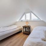 Zwei Betten in einem Dachzimmer mit Dachfenster und Holzboden.
