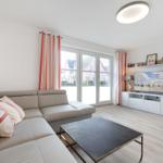 Wohnzimmer mit Sofa, Couchtisch und TV. Fenster mit Vorhängen. Holzboden.