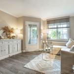 Wohnzimmer mit Sofa, Sideboard und Fenster. Holzboden und Beleuchtung.